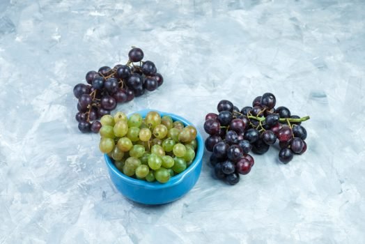 grape bunches in a bowl high angle view on a grungy grey background grape bunches in a bowl high angle view on a grungy grey background