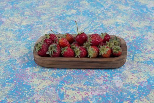Red strawberries in a wooden platter on the blue table Red strawberries in a wooden platter on the blue table. High quality photo