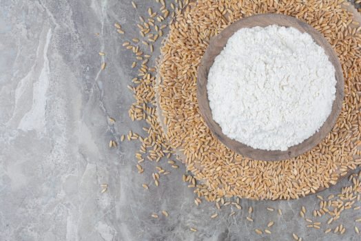 A wooden bowl with flour and oat grains on marble background A wooden bowl with flour and oat grains on marble background. High quality photo